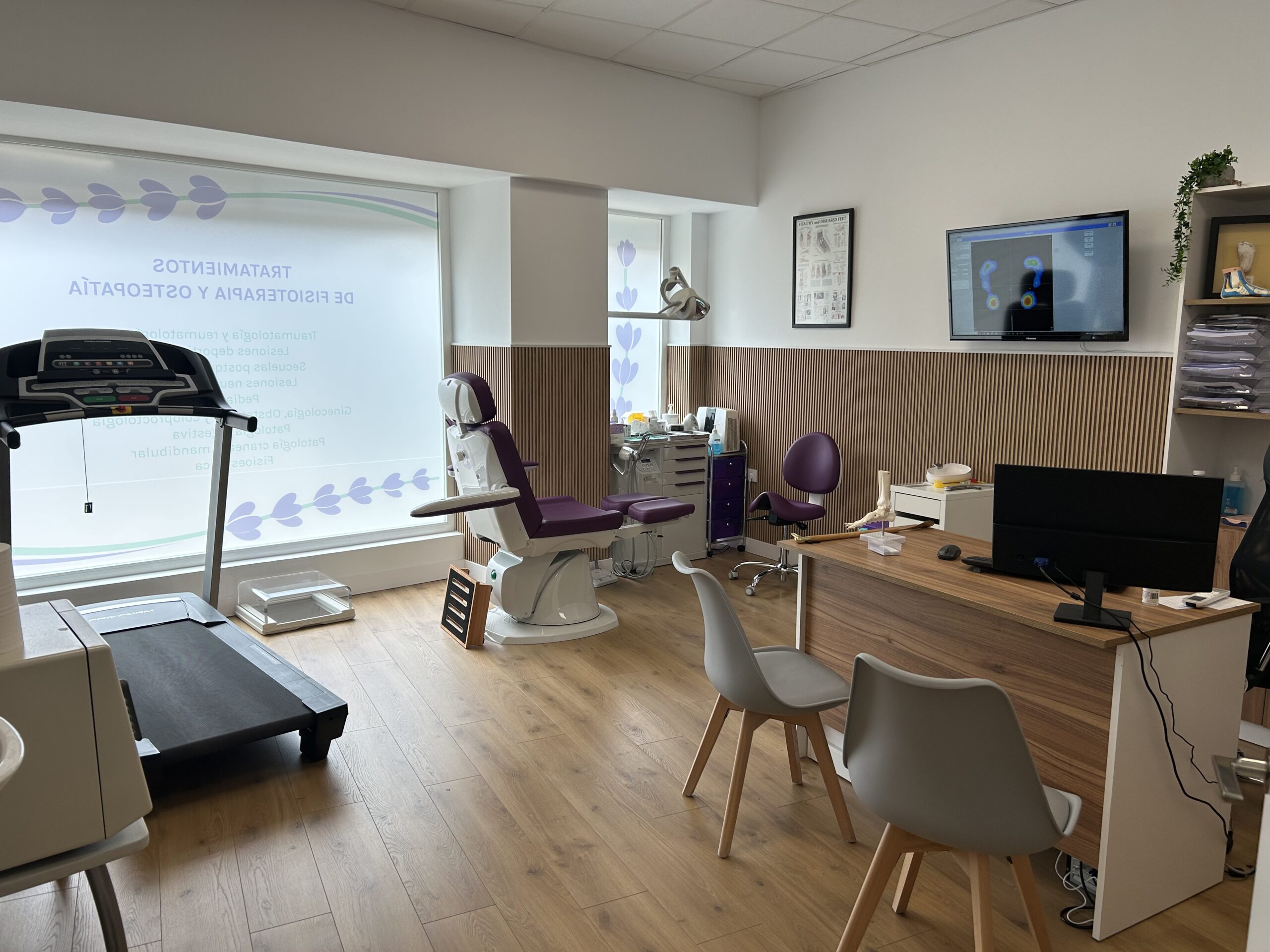 Clínica equipada con sillón podológico, escritorio y cinta de correr, mostrando un ambiente cuidado y profesional.