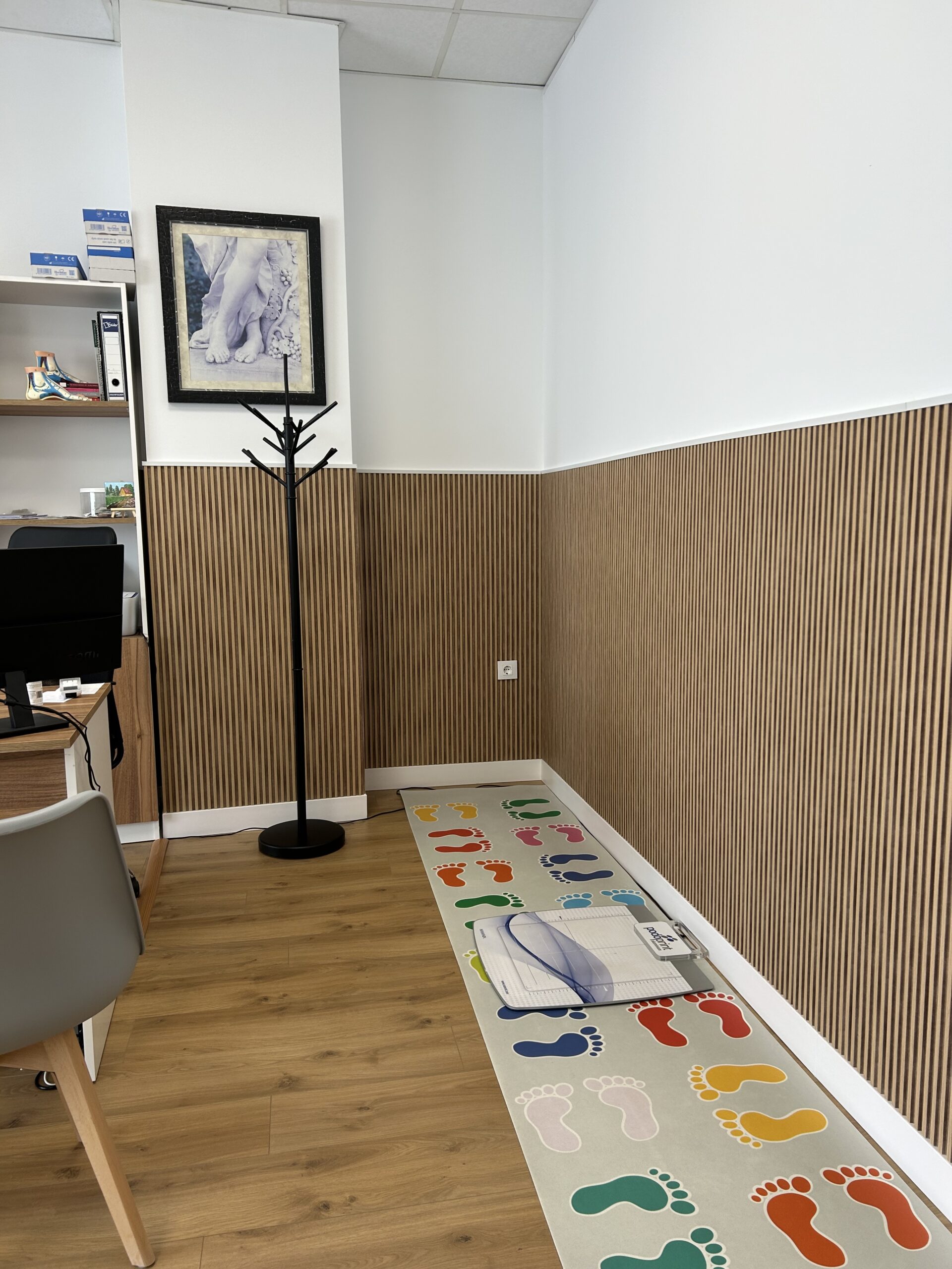 Rincón de la clínica con alfombra decorada con huellas de colores y un escáner para el estudio de la pisada.